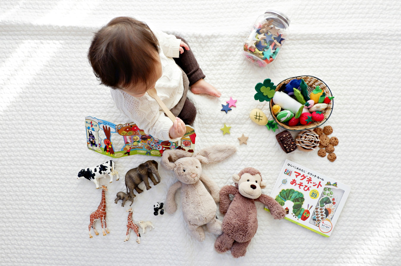 Happy baby sitting on the floor smiling while playing with colorful educational toys in a bright indoor room, representing baby toys, learning, and kids' essentials.