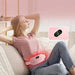 Woman wearing pink portable massage heating belt for back pain relief; reusable heat wrap with remote on couch